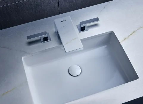 Ein rechteckiges, eingelassenes Waschbecken mit einer glänzenden, weißen Oberfläche, eingebettet in eine Marmorplatte mit feiner Aderung.