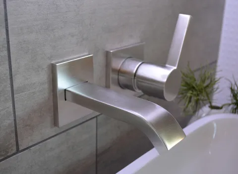 Eine moderne Wandarmatur aus gebürstetem Edelstahl ist an einer grau gefliesten Wand über einer Badewanne installiert.