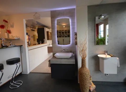 Ein modernes Gästebad zeigt ein weißes, wandhängendes Waschbecken mit abgerundeter Form vor einer grauen Betonoptik-Wand. 