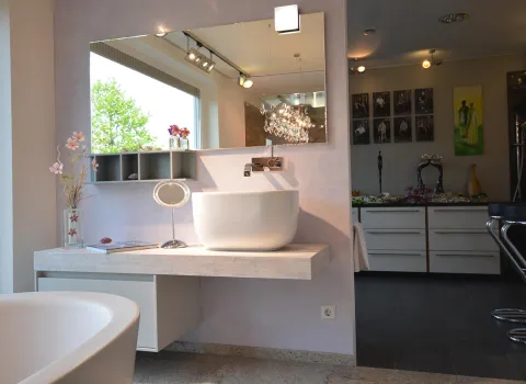 Ein modernes Badezimmer mit einem freistehenden, ovalen Waschbecken auf einer schwebenden Holzplatte vor einer pastellfarbenen Wand.