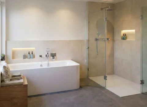 Badezimmer mit einer geräumigen Dusche und separater Badewanne. Beleuchtete Wandnischen neben beiden Bereichen setzen Pflegeprodukte stilvoll in Szene.