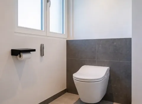 Wandhängendes WC mit grauen Steinoberflächen und natürlichem Lichteinfall
