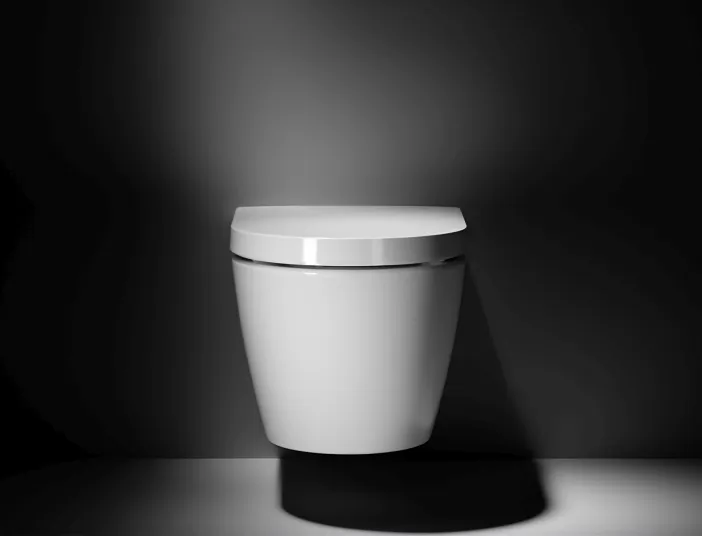 Ein elegantes, wandmontiertes Duravit-WC der Serie ME Hero Edition mit geschwungener Frontansicht präsentiert sich vor einer dramatisch beleuchteten Wand.