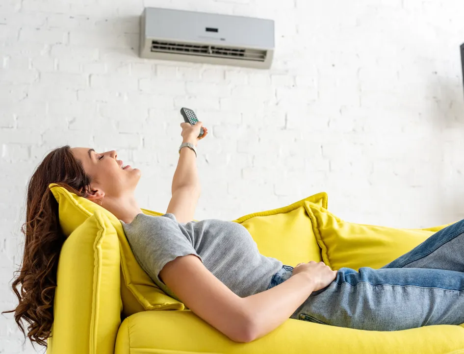 Frau auf dem Sofa bedient eine Klimaanlage per Fernbedienung